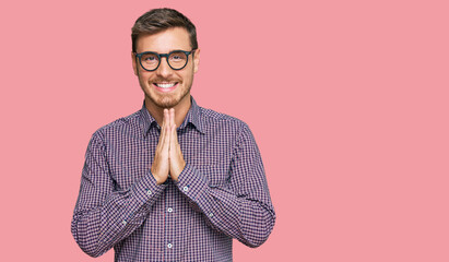 Handsome caucasian man wearing casual clothes and glasses praying with hands together asking for forgiveness smiling confident.