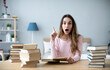 © BestForYou - Young alarmed woman student with many books points up. Learning at home.