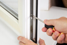 Handyman Adjusting White Pvc Plastic Window Indoors. Worker Using Screwdriver To Repair Upvc Window. Homework Maintenance