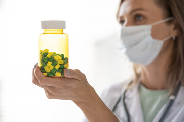 Poster - Hand of young contemporary doctor in protective mask holding bottle with pills