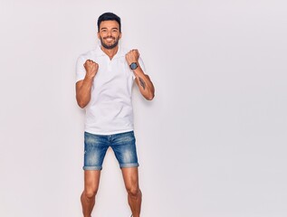 Young handsome hispanic man wearing casual clothes smiling happy. Jumping with smile on face celebrating with fists up over isolated white background