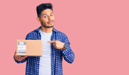 Handsome latin american young man holding delivery package smiling happy pointing with hand and finger