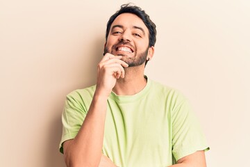 Young hispanic man wearing casual clothes smiling looking confident at the camera with crossed arms and hand on chin. thinking positive.