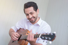 Happy Man Playing Guitar While Sitting On Sofa In Living Room, Enjoying Carefree Time At Home.