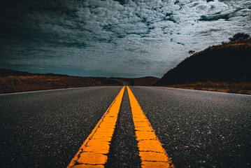 Perspective view of yellow lane lines of an old asphalt road through the field and clouds on blue sky in summer day