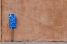 Abstract Background Of An Exterior Reddish Brown Adobe Style Textured Wall Surface, With View Of A Handicap Parking Sign
