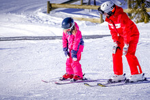 L'Alpe D'Huez, France 02.01.2019 Professional Ski Instructor Is Teaching A Child To Ski On A Sunny Day On A Mountain Slope Resort. Family And Children Active Vacation.