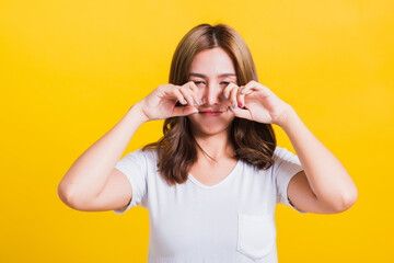 Wall Mural - Asian Thai portrait beautiful cute young woman in depressed bad mood her cry wipe tears with fingers, studio shot isolated on yellow background with copy space