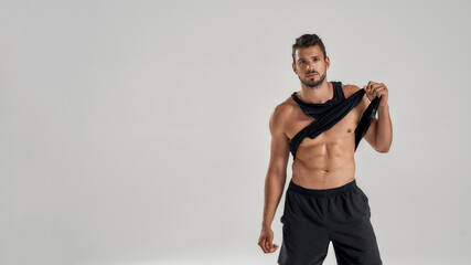 Wall Mural - Young handsome muscular caucasian man looking at camera, lifting black shirt, showing his abs while posing isolated over grey background