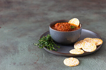 Ceramic bowl with spicy tomato sauce, tortilla chips and thyme on green stone background. Mexican food concept.