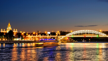 Wall Mural - downtown moscow city skyline at night. Historic architecture landmark with Moscow university building and railway bridge reflection on moscow river water against dusk sky background. Wide panorama