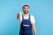 © khosrork - Hey you! Portrait of happy handyman in overalls and gloves, pointing finger to camera. Profession of service industry, builder and house maintenance. Expert repairman in workwear making choice