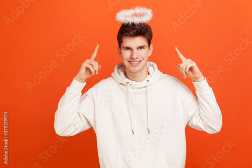 Fotografía Handsome innocent young man in casual sweatshirt pointing fingers on fluffy nimbus overhead and smiling, blessing