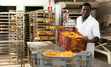 Professional African American Baker Working In Bakehouse, Carrying Box With Baked Bread..