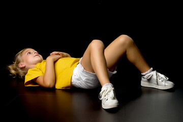 cute little girl lying on the floor in the studio on a black background