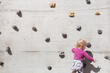 Little child in front of climbing wall outdoors on a light gray concrete surface. Kleines Kind vor Kletterwand im freien auf einer hellgrauen Betonoberfläche.