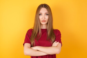 Beautiful Young beautiful caucasian girl wearing red t-shirt over isolated yellow background serious face with crossed arms looking at the camera. Positive person.