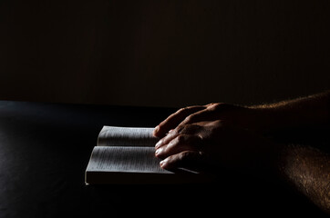 Wall Mural - Closeup of male hands on the opened Bible, dark atmosphere