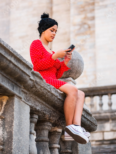 Cuadros en Lienzo An attractive young female looking at her smartphone while sitting on a stone ba