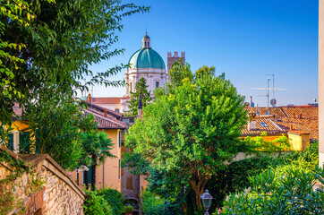 Wall Mural - Dome of Santa Maria Assunta New Cathedral, Duomo Nuovo Roman Catholic church, tiled roofs of old buildings and green trees, Brescia city historical centre, blue sky, Lombardy, Northern Italy