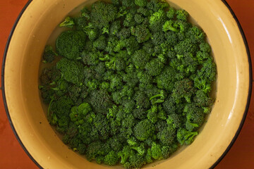 Wall Mural - Inflorescences of broccoli cabbage in a yellow basin on a brown background. Green vegetables, harvest. Texture, copy space, top view.