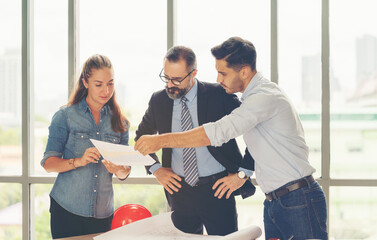 Wall Mural - Team of multiethnic architects working on construction plans in meeting room. Engineers discussing on project in office. Mature businessman and woman standing around table working on blueprint.