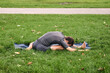 © OneWellStudio - Young athletic man in sportswear doing yoga in the park. Practice Janu Sirshasana asana head to knee pose outdoors. People exercising stretching on green grass with yoga mat.