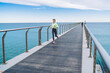 © BullRun - Strong female jogger in stylish tracksuit enjoying morning run across seashore boardwalk, Caucasian athlete in good shape running with motivation at coastline pier keeping healthy lifestyle