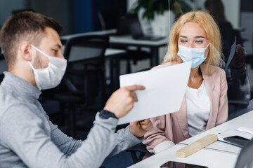 Wall Mural - Working with graphs and diagrams during social distance. Busy young man and woman managers in protective masks work with documents through glass board