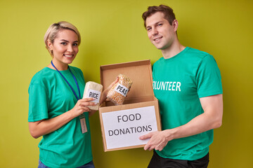 Wall Mural - portrait of young caucasian couple collecting donation for poor, hold box with cereals isolated over green background