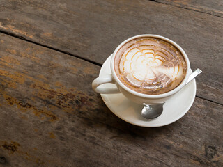 hot latte coffee and bubble in white coffee cup and saucer with a spoon on wooden background.