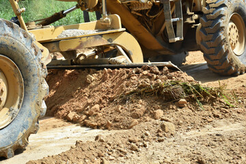 A pile of soil with blade of motor grader machine work for clearing ground level before soil filling for making to rural road.