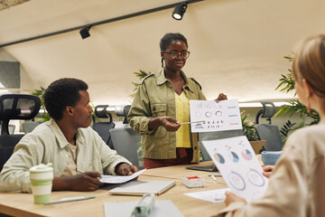 Wall Mural - portrait of young african-american woman holding data chart while giving report of statistics and pe