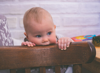 Little pensive child sitting in a vintage brown chair biting the back of the chair