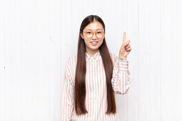 Wall Mural - asian young woman smiling cheerfully and happily, pointing upwards with one hand to copy space