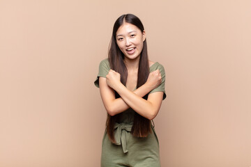 Wall Mural - asian young woman smiling cheerfully and celebrating, with fists clenched and arms crossed, feeling happy and positive