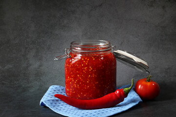 Ground hot red pepper with tomatoes in a glass jar on a dark background. A spicy seasoning made from pepper and tomatoes at home. Home cooking.