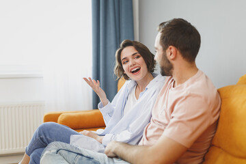 Wall Mural - Excited cheerful funny young couple two friends man woman 20s in casual clothes sitting on couch hugging speaking talking looking at each other resting relaxing spending time in living room at home.