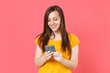 © ViDi Studio - Smiling beautiful attractive young brunette woman 20s wearing yellow casual t-shirt posing standing using mobile cell phone typing sms message isolated on pink color wall background studio portrait.