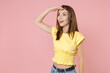 © ViDi Studio - Excited cheerful young brunette woman 20s wearing yellow casual t-shirt posing standing holding hand at forehead looking far away distance isolated on pastel pink color background studio portrait.