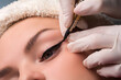 Permanent eye makeup close up shot. Cosmetologist applying tattooing of eyes. Makeup eyeliner procedure