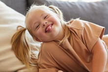 Portrait Of Carefree Little Girl With Down Syndrome Sticking Tongue Out While Grimacing For Camera