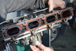 A car mechanic holds an intake manifold from a car engine