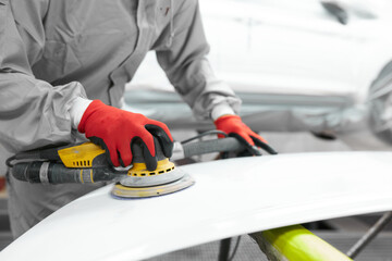 young caucasian professional car service male worker with orbital polisher, male polishing car body in auto repair shop