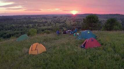 Wall Mural - Camping family aerial. Extended family sit on the coast of the river with hiking camps set around and enjoy gentle sunset.