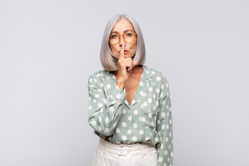 Wall Mural - gray haired woman looking serious and cross with finger pressed to lips demanding silence or quiet, keeping a secret