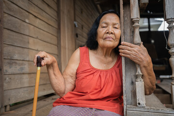 Wall Mural - Thai elderly woman in round-necked sleeveless collar sitting lonely in wooden home