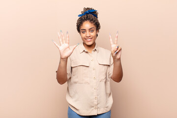 young afro woman smiling and looking friendly, showing number seven or seventh with hand forward, counting down