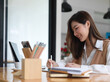© bongkarn - Portrait of smiling female university student doing assignment with digital devices and stationery