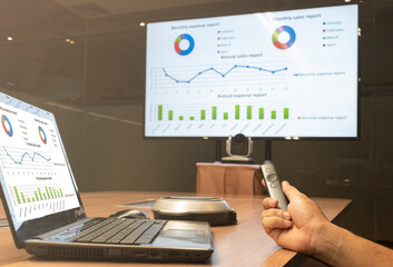 Businessman hand hold remote control with mockup presentation silde show on display laptop and television in meeting room